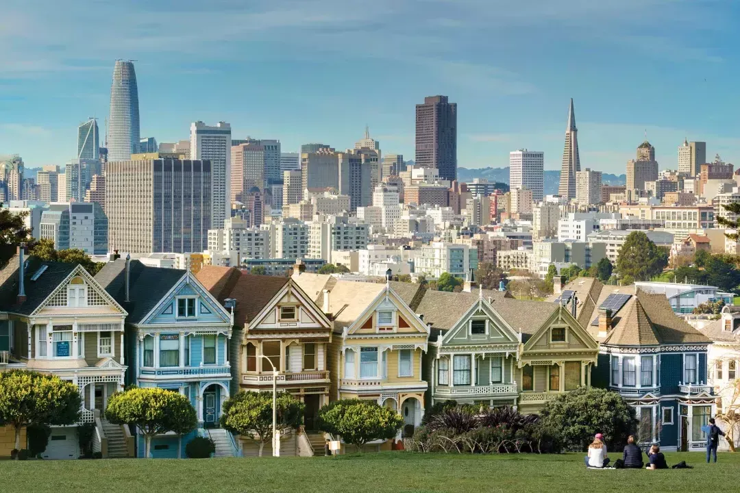 Picknicker sitzen im Gras im Alamo Square Park mit den Painted Ladies und der Skyline von San Francisco im Hintergrund.